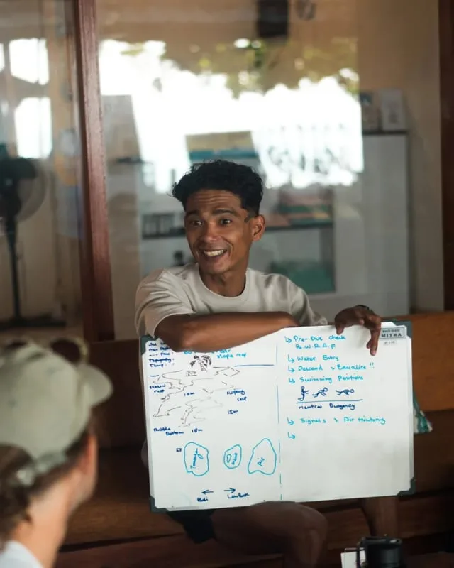 Instructeur de plongée souriant expliquant des signaux avec un tableau blanc