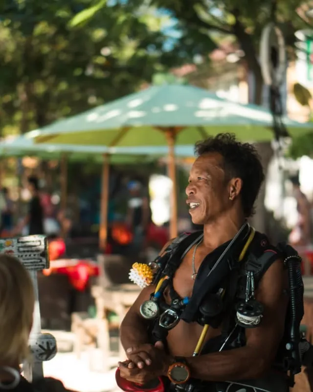 Plongeur souriant avec son équipement complet près d'un parasol vert