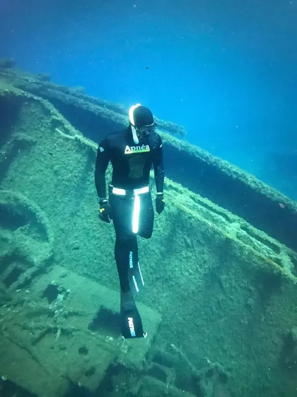 Apnéiste en combinaison noire descendant le long d'une épave sous-marine