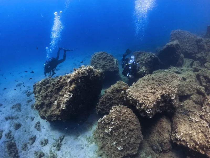 Deux plongeurs explorent un fond marin rocheux et bleu clair