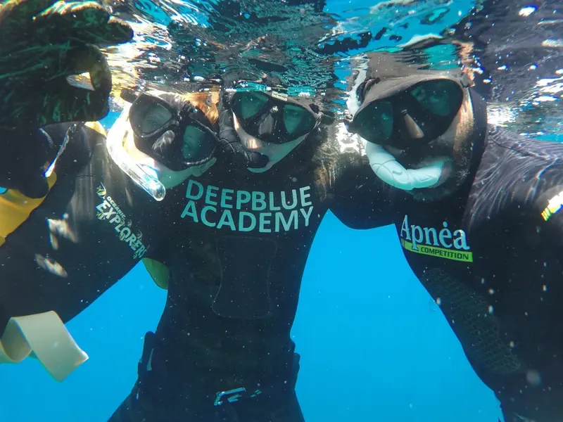 Trois plongeurs en apnée sourient à la caméra sous l'eau