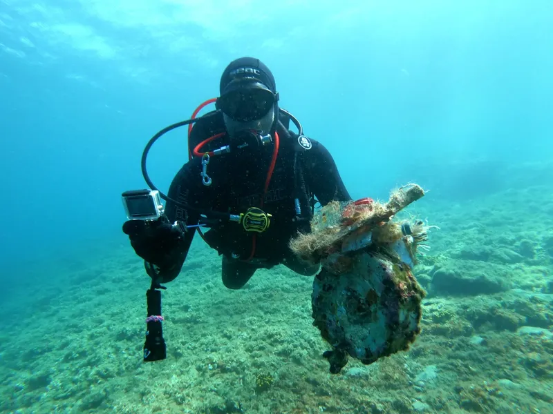 Plongeur en combinaison noire manipule un objet ancien sur le fond marin