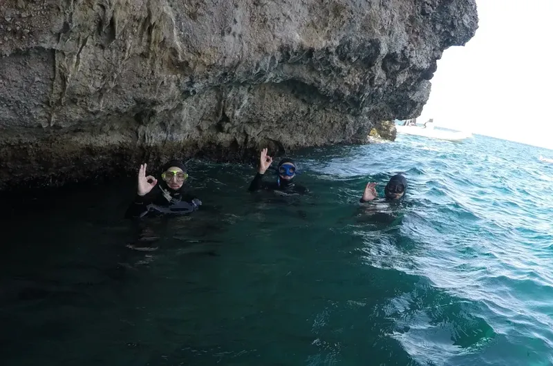 Trois plongeurs souriants font un signe OK sous une falaise rocheuse