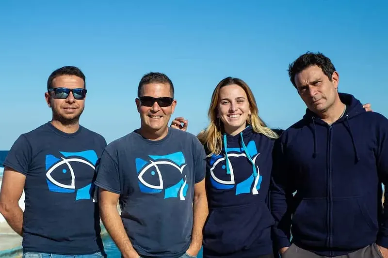 Quatre personnes souriantes, portant des vêtements bleus avec un motif de poisson