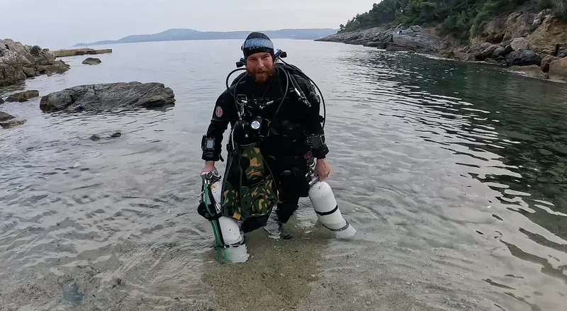 Plongeur équipé se tient dans l'eau peu profonde sur une plage
