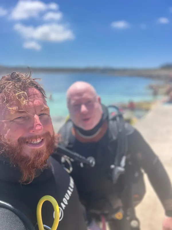 Deux plongeurs souriants en immersion dans une eau turquoise claire