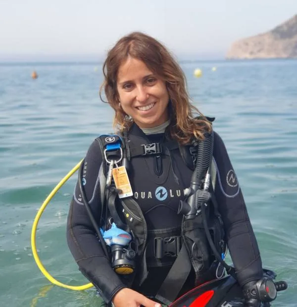 Plongeuse souriante en combinaison, équipement complet, mer calme en arrière-plan