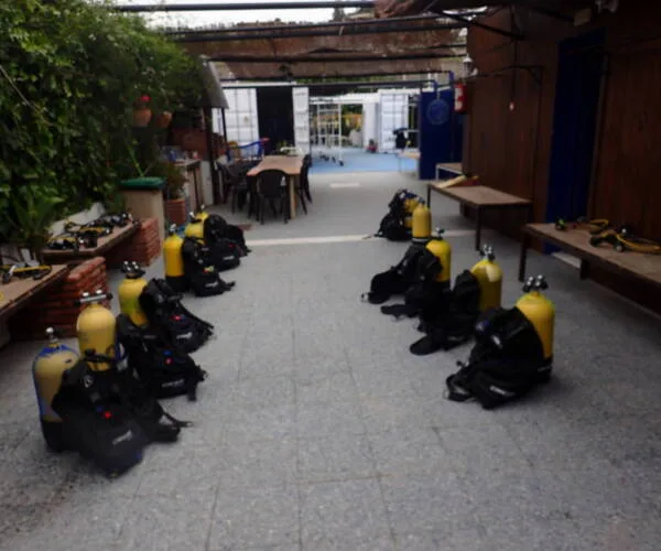Bouteilles de plongée alignées sur une cour ombragée avec tables et chaises