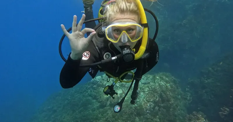 Plongeuse souriante avec signe OK, en combinaison, dans l'eau bleue