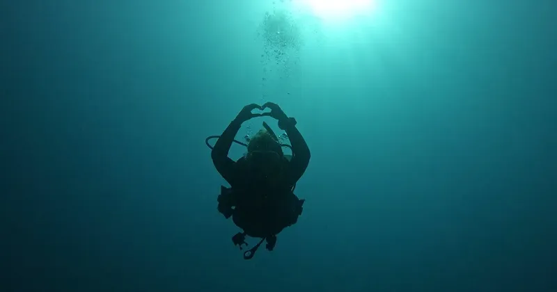 Plongeur en scaphandre forme un cœur avec ses mains sous l'eau
