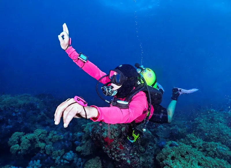 Plongeur pointant vers le haut dans l'eau bleue avec équipement complet