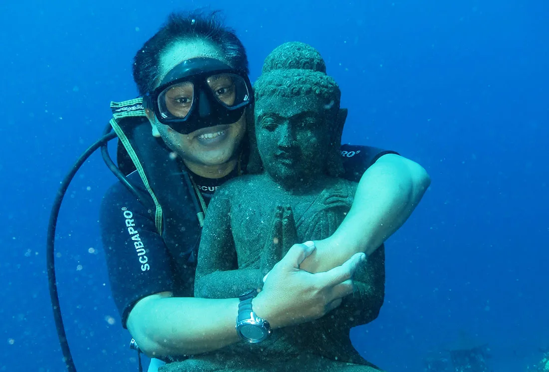 Plongeuse souriante étreint une statue de Bouddha sous l'eau