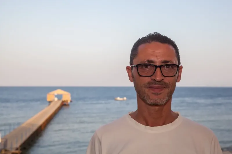 Homme souriant avec lunettes devant la mer et un ponton