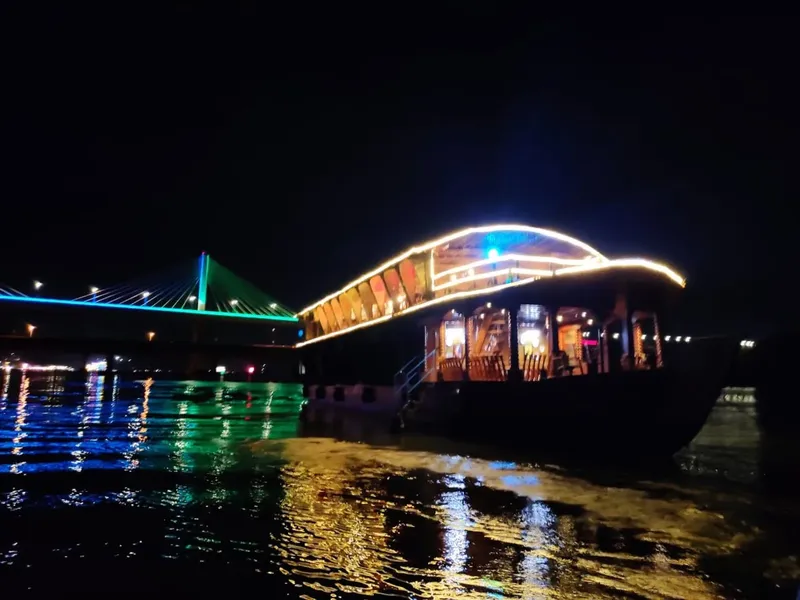 Bateau illuminé la nuit avec un pont en arrière-plan