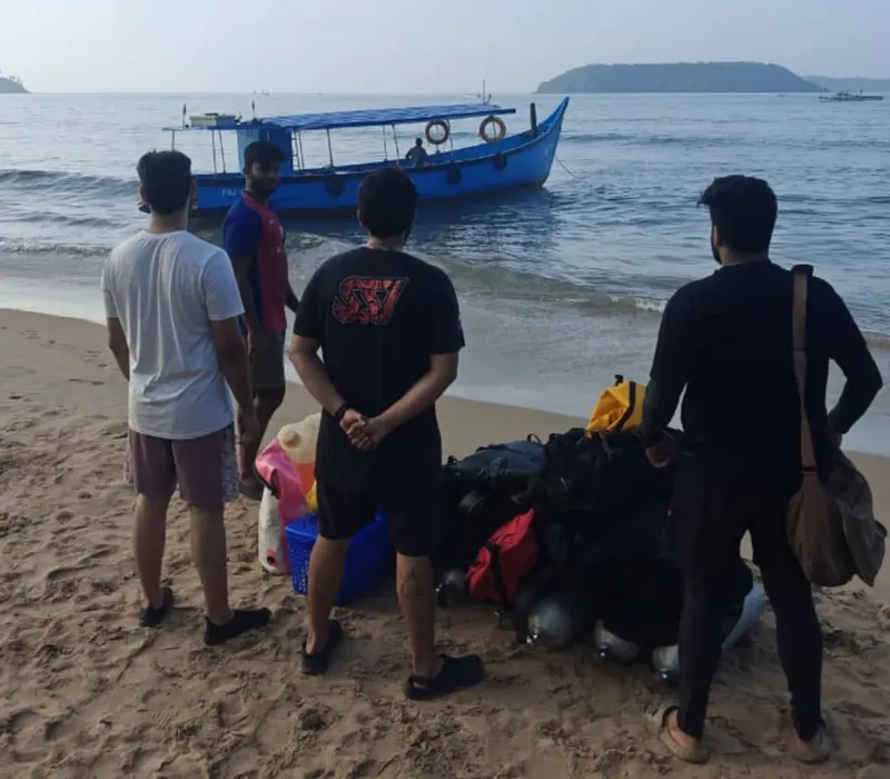 Plongée : groupe de personnes sur une plage avec un bateau bleu