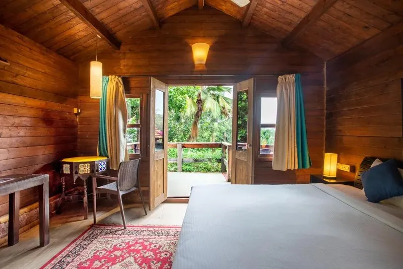 Chambre en bois avec lit, bureau et vue sur la végétation tropicale