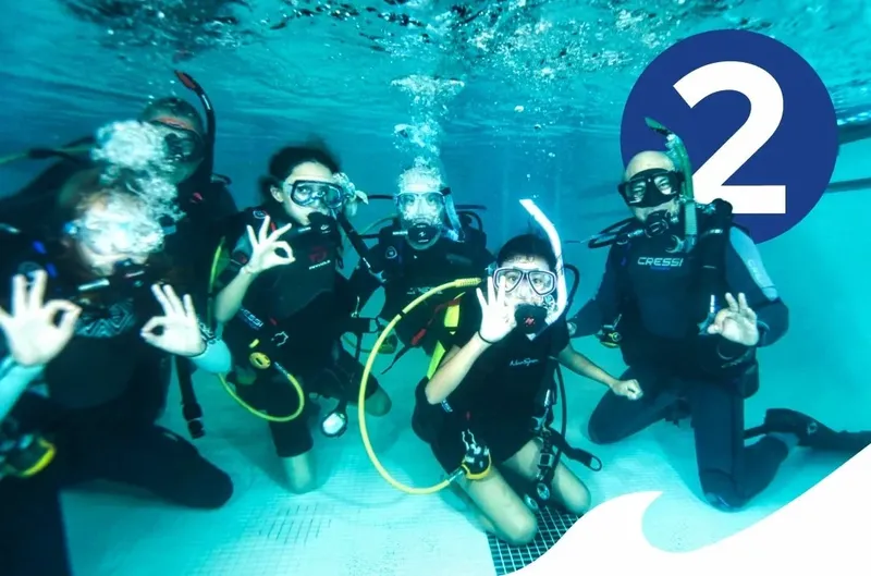 Groupe de plongeurs souriants, faisant des signes, dans une piscine