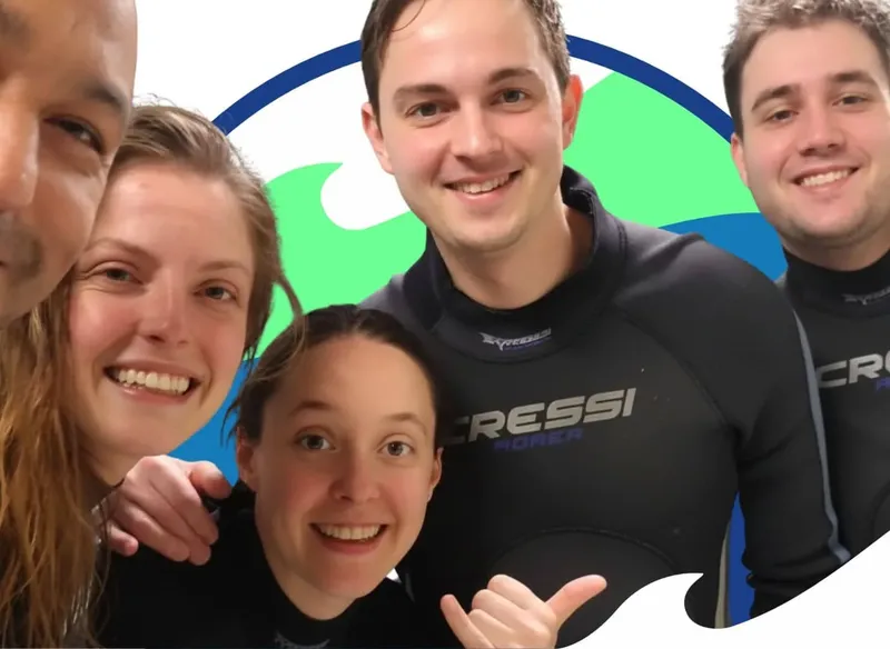 Quatre personnes souriantes en combinaison de plongée, regardant la caméra