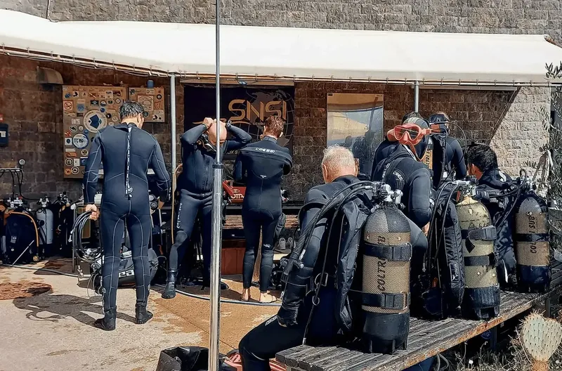 Plongeurs en combinaison se préparent avec leur équipement devant un bâtiment