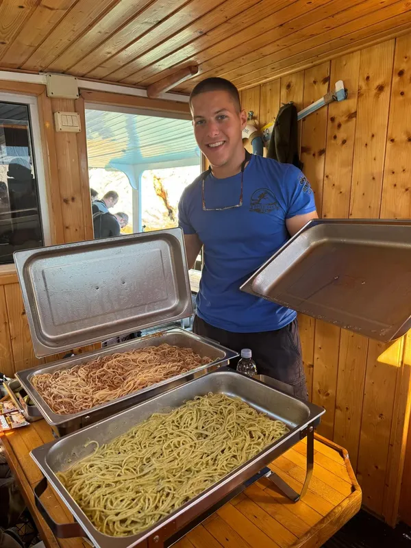 Un homme souriant présente des plats de pâtes sur un bateau