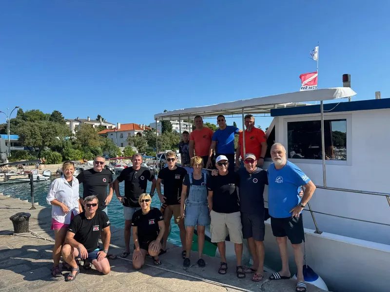 Groupe de plongeurs souriants posent devant un bateau amarré au port