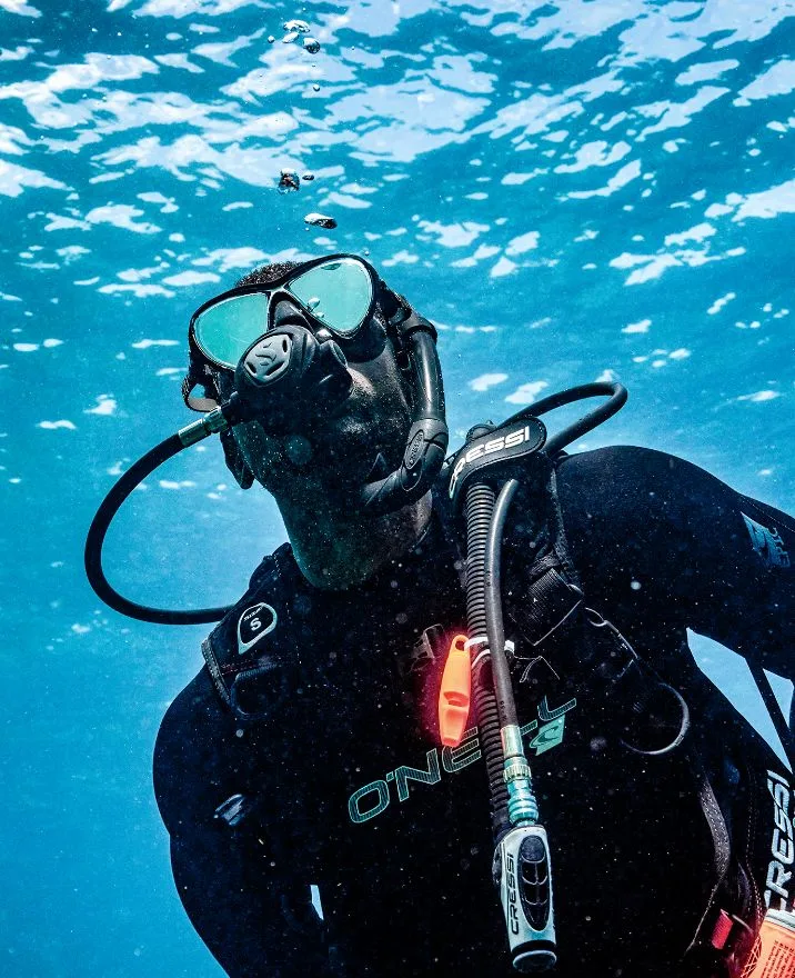 Plongeur en combinaison noire, masque et détendeur, sous l'eau turquoise