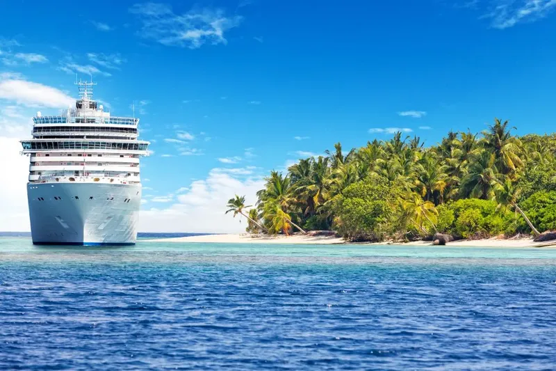 Grand paquebot blanc devant une île tropicale et lagon turquoise