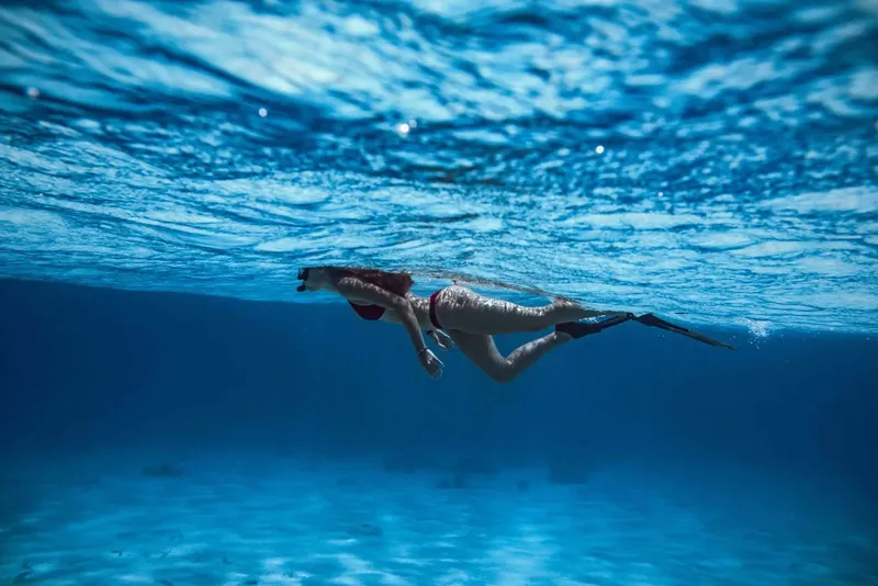 Femme nageant en apnée dans une eau bleue claire et limpide