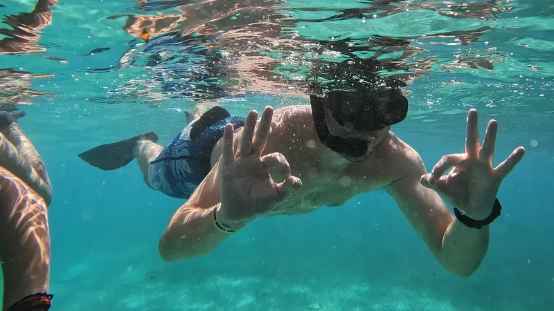 Plongeur souriant avec signe OK, nageant dans une eau turquoise claire