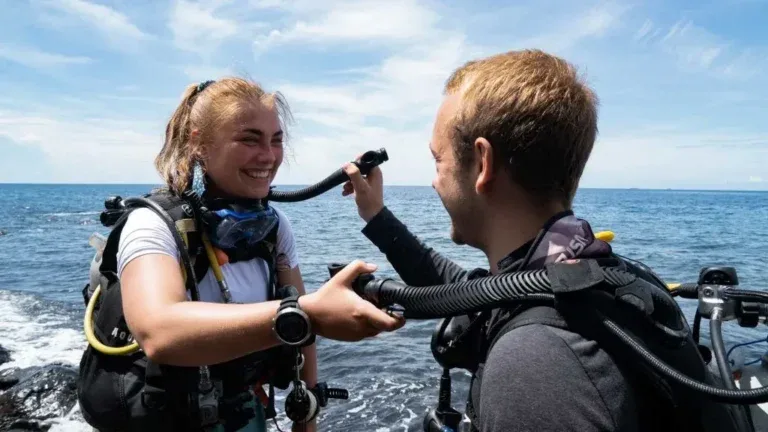 Deux plongeurs souriants s'équipent sur un bateau en mer