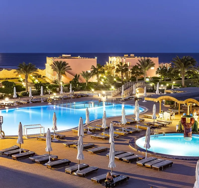 Vue nocturne d'un complexe hôtelier avec piscines et transats éclairés