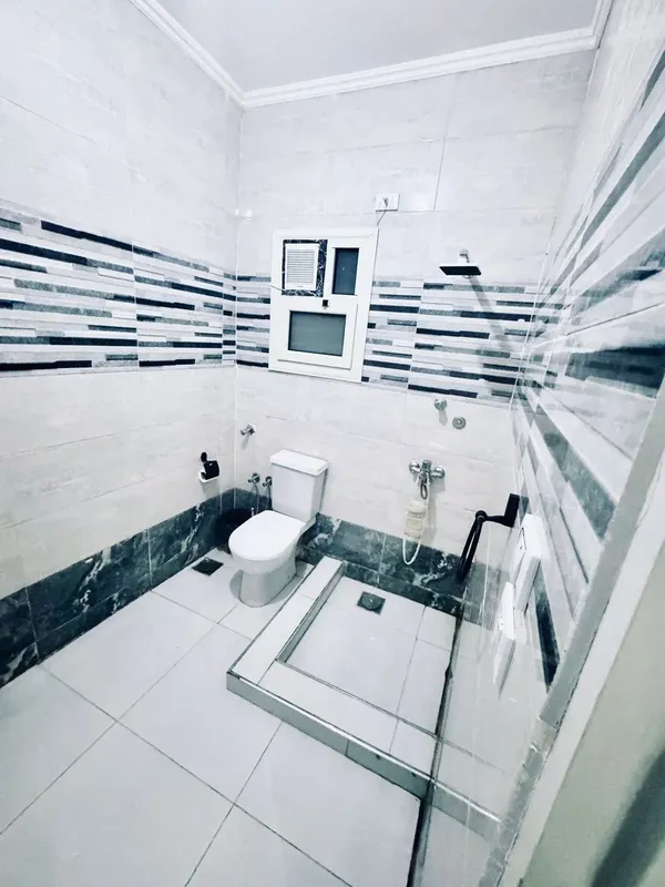 Salle de bain carree avec douche, toilettes et carrelage noir et blanc