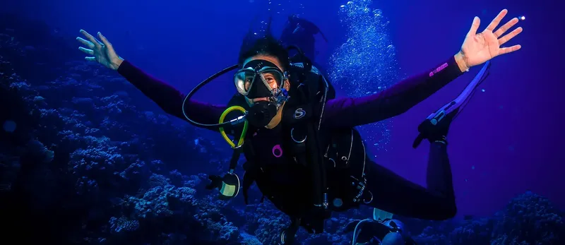 Plongeuse en combinaison explore les fonds marins avec les bras ouverts