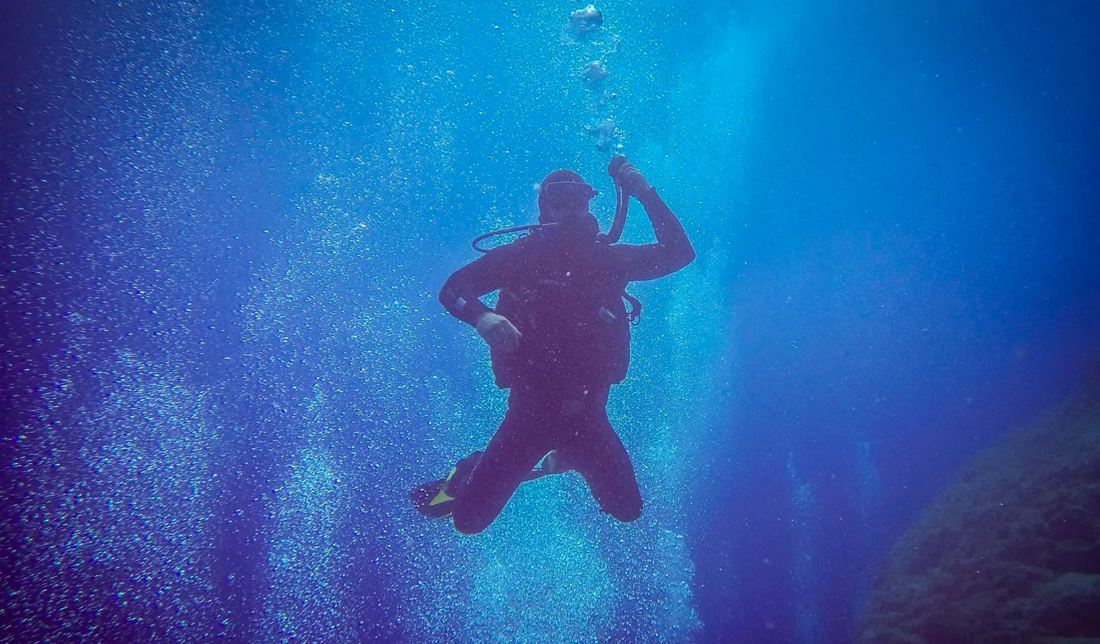 Plongeur en combinaison noire descendant dans une eau bleue claire