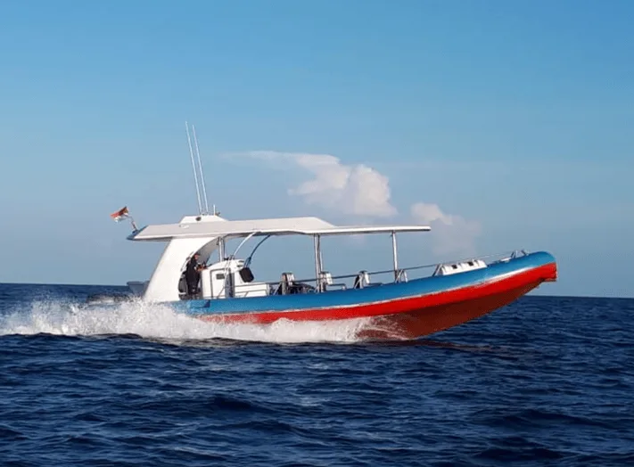 Bateau de plongée bleu et rouge navigue sur une mer calme