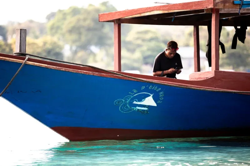 Homme sur un bateau bleu, regardant son téléphone portable en mer