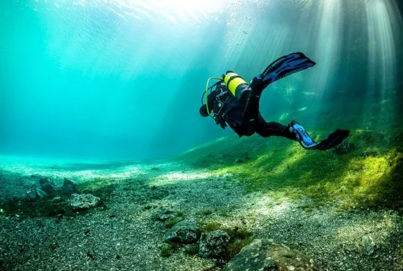 Plongeur en scaphandre nageant dans une eau turquoise et lumineuse
