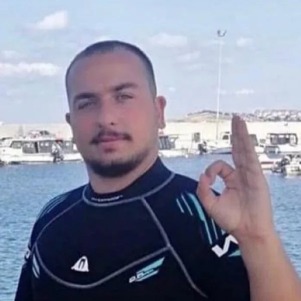 Plongeur en combinaison fait un signe OK devant des bateaux amarrés