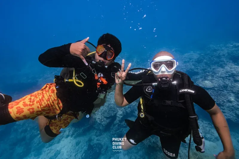 Deux plongeurs souriants font des signes de la main sous l'eau