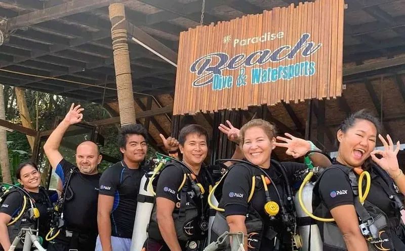 Groupe de plongeurs souriants devant l'enseigne d'un centre de plongée