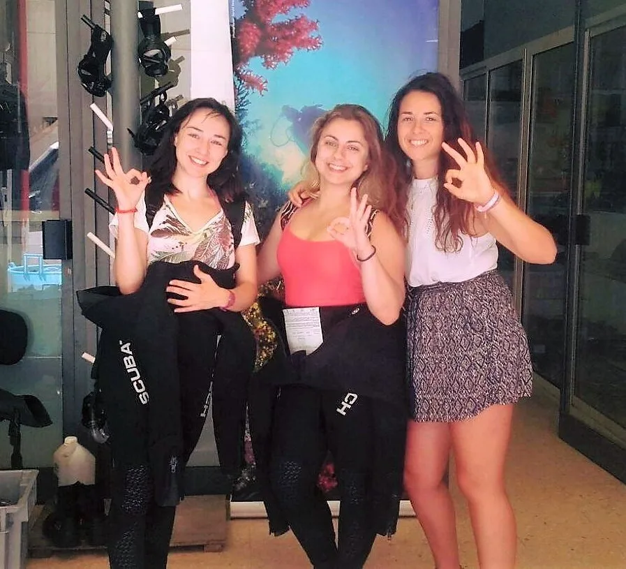 Trois plongeuses souriantes font un signe OK devant du matériel