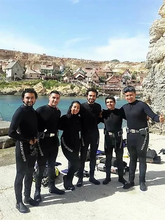Groupe de plongeurs souriants en combinaison sur un quai rocheux