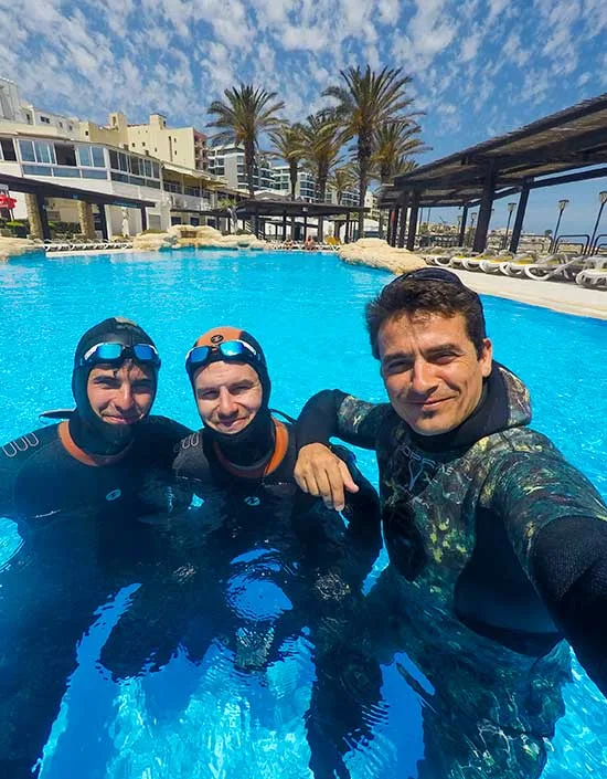 Trois personnes souriantes en combinaison de plongée dans une piscine