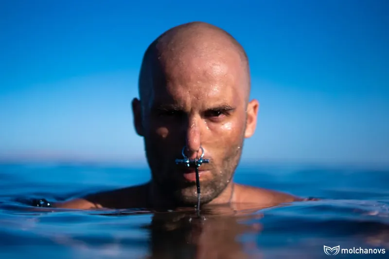 Homme à la tête rasée émerge de l'eau, regard intense et masque