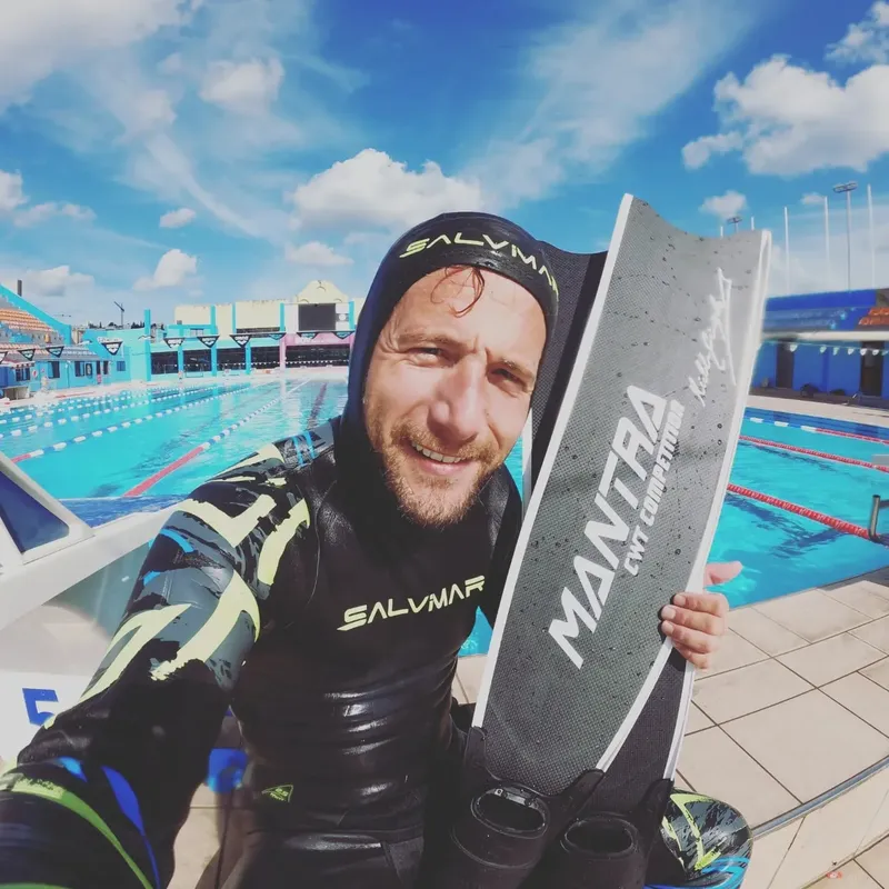 Apnea, un homme en combinaison noire tient une planche de plongée