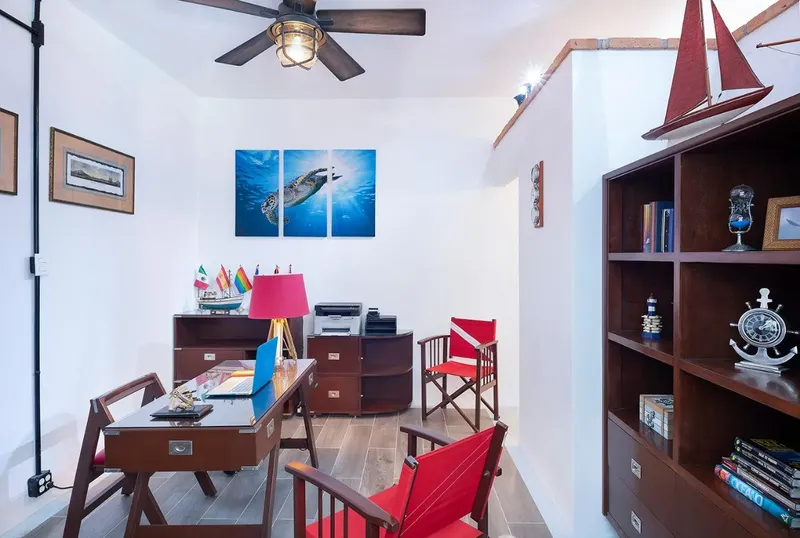 Bureau avec décoration marine, bibliothèque, chaises rouges et ventilateur de plafond