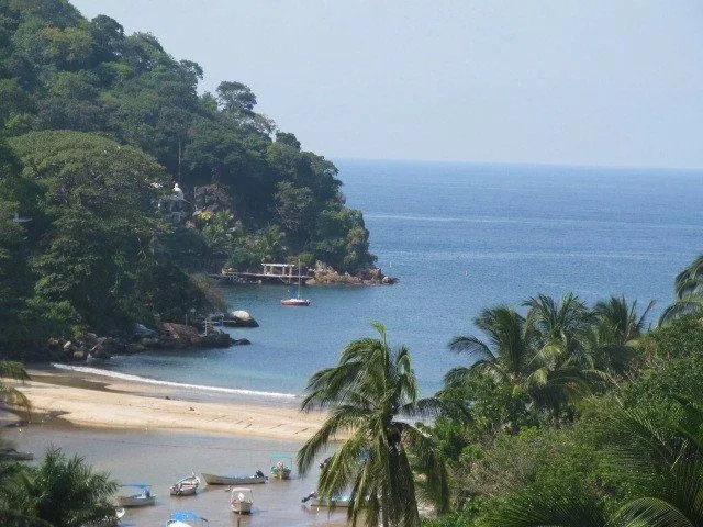 Plage de sable, mer bleue, végétation luxuriante et quelques bateaux amarrés