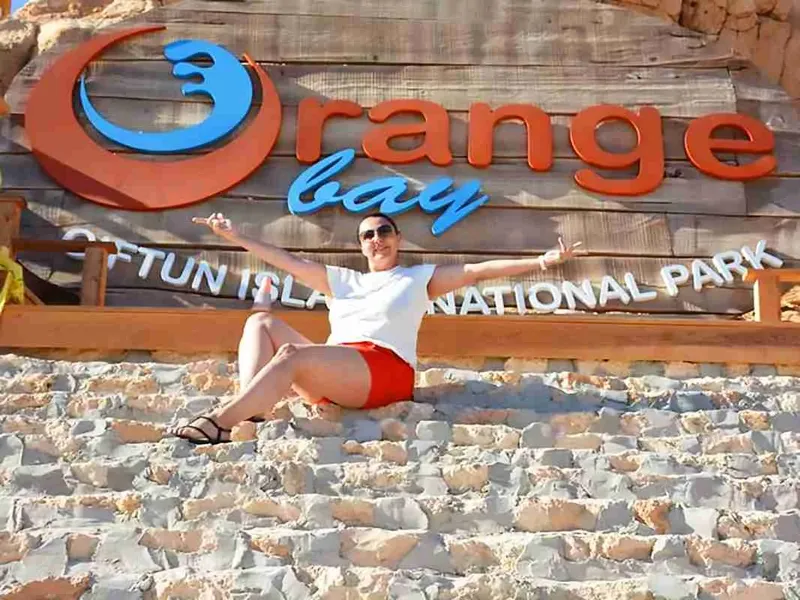 Femme souriante se relaxe devant une enseigne colorée en bord de mer