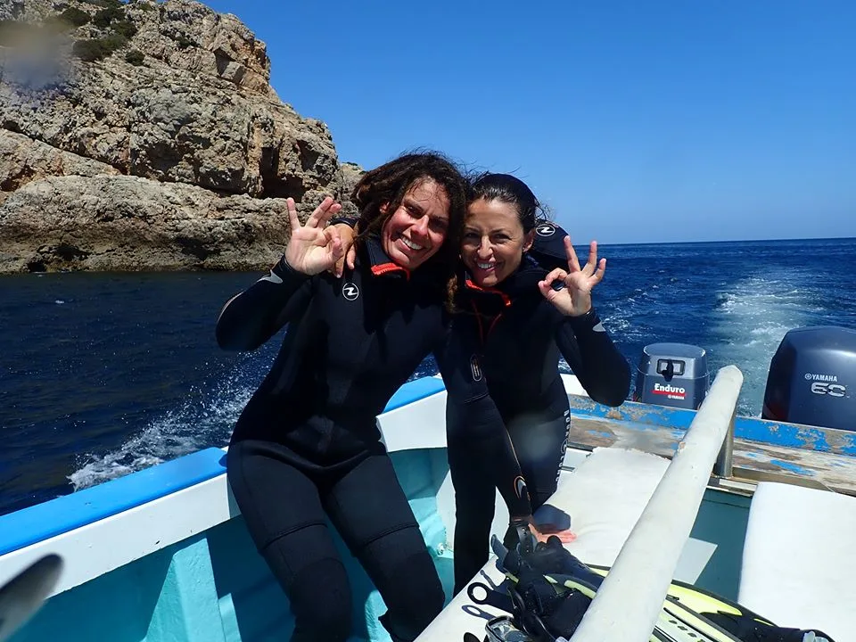Deux plongeuses souriantes font des signes de victoire sur un bateau