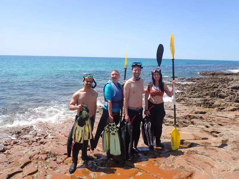 Quatre personnes souriantes avec palmes et masques sur une plage rocheuse